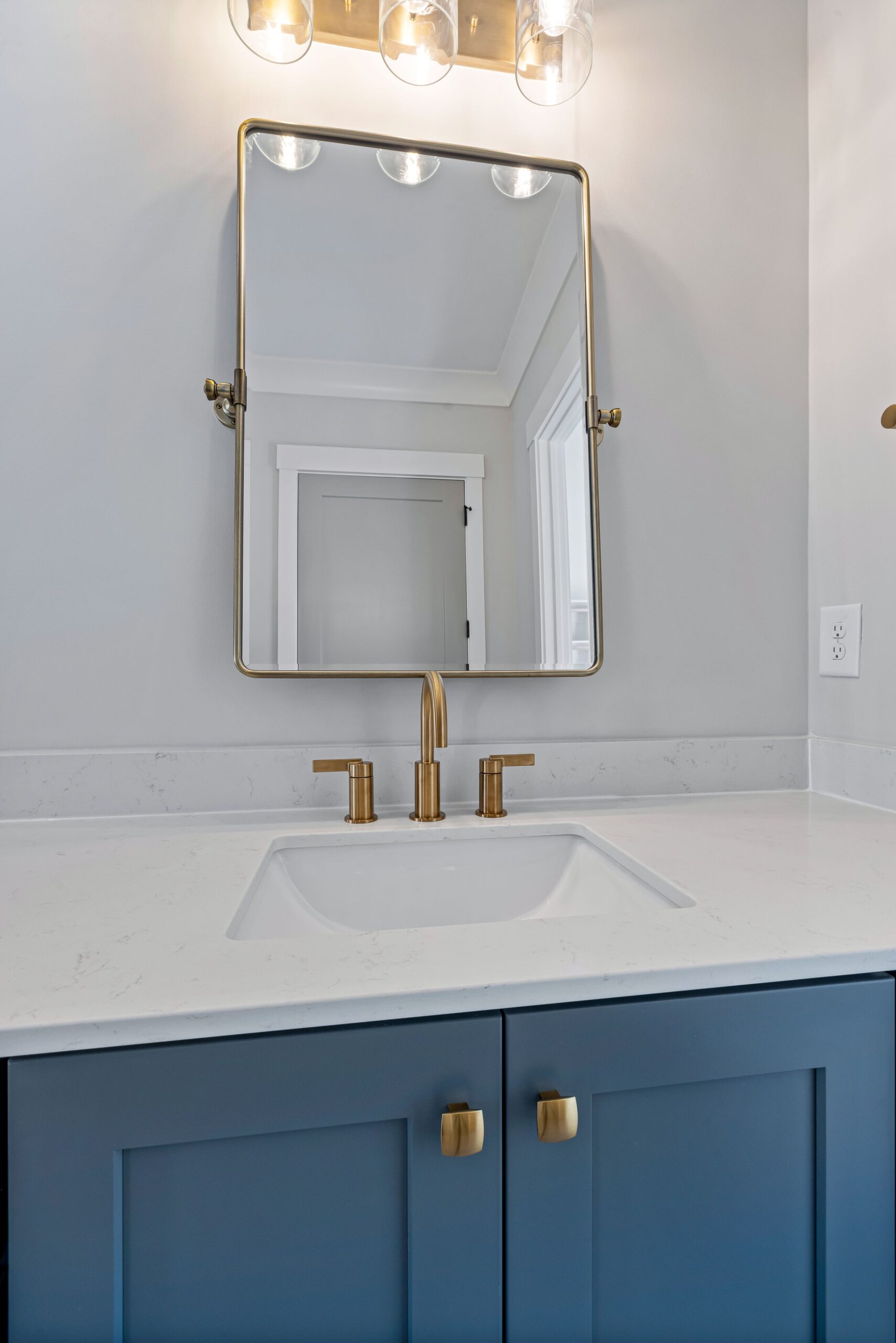 Blue shaker bathroom vanity with brass knobs and a white countertop