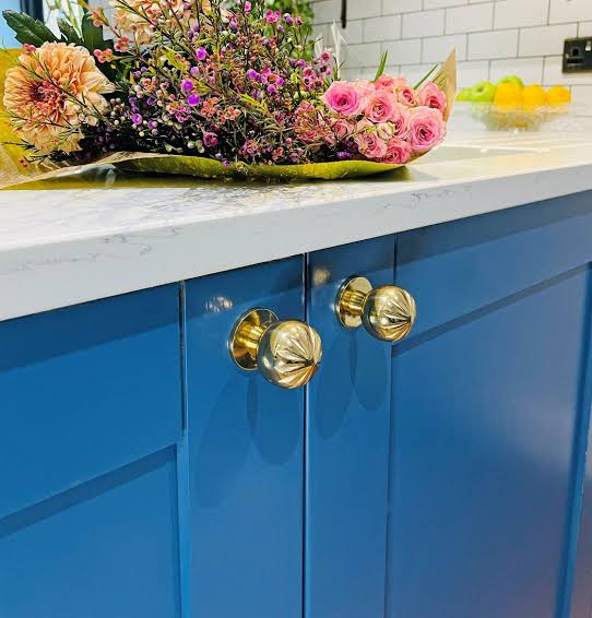 Hardware 4 Round brass knobs on sage green and cream shaker kitchen cabinets with a stone backsplash