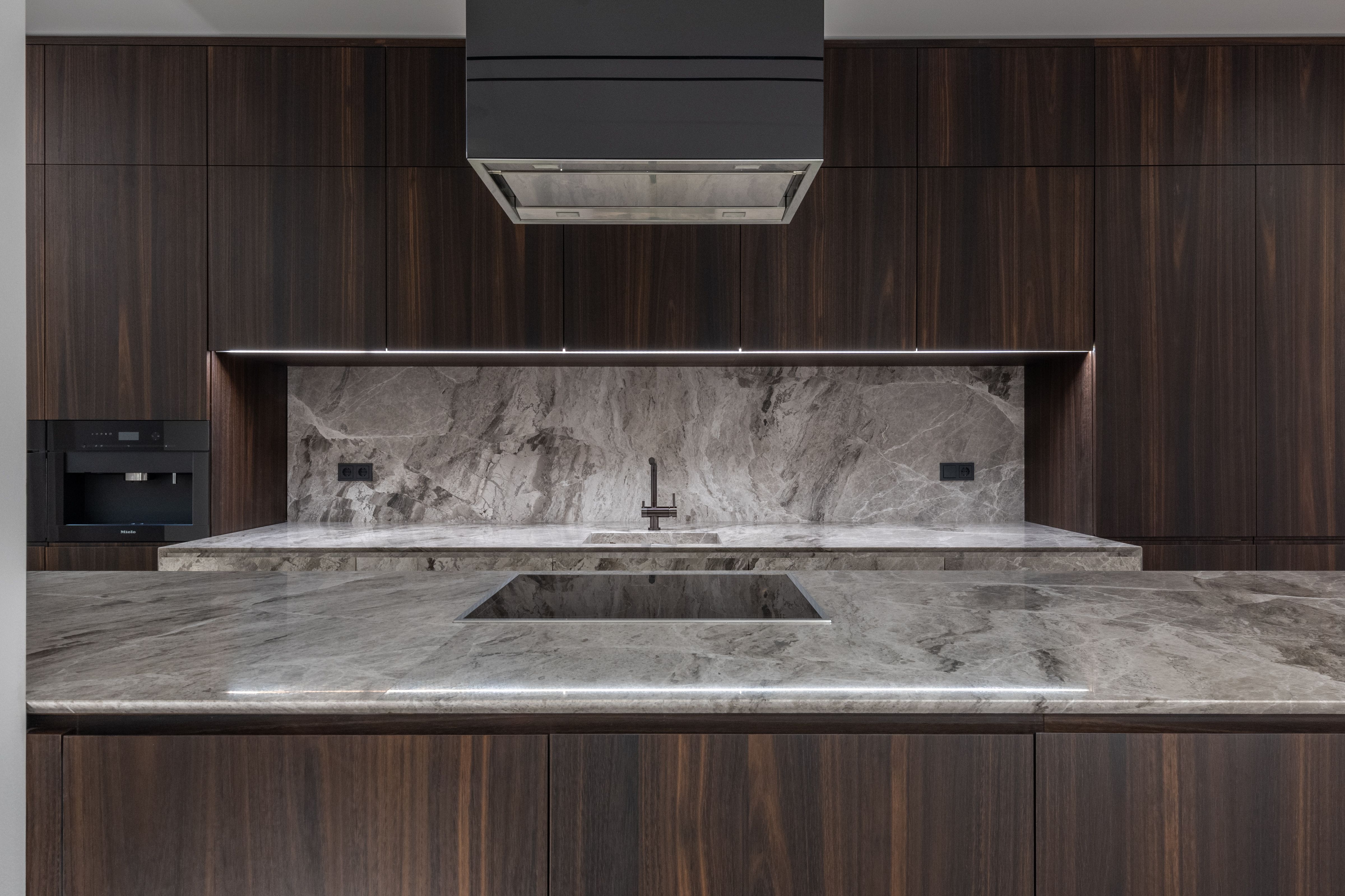 Gray-veined stone countertop and full-height backsplash with a cooktop in a dark wood kitchen