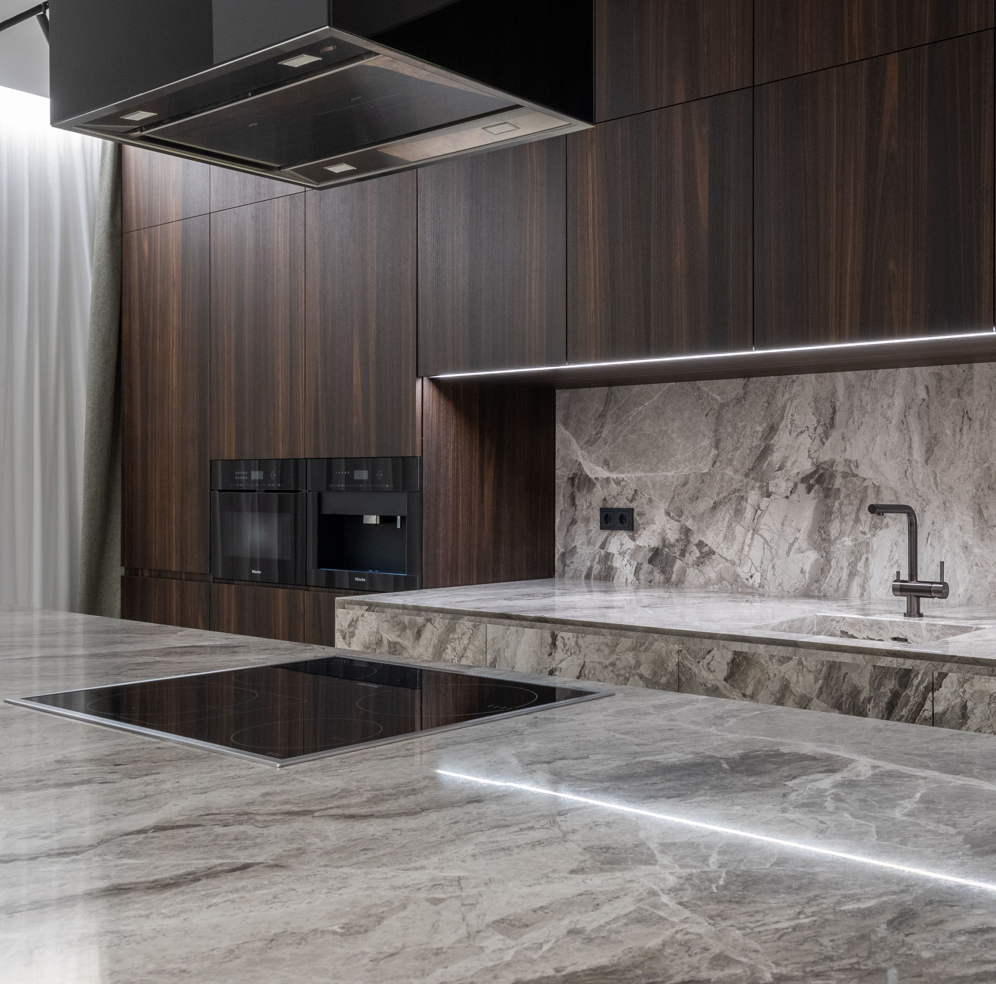 Kitchen island with a gray-veined stone countertop and matching backsplash in front of dark wood cabinets