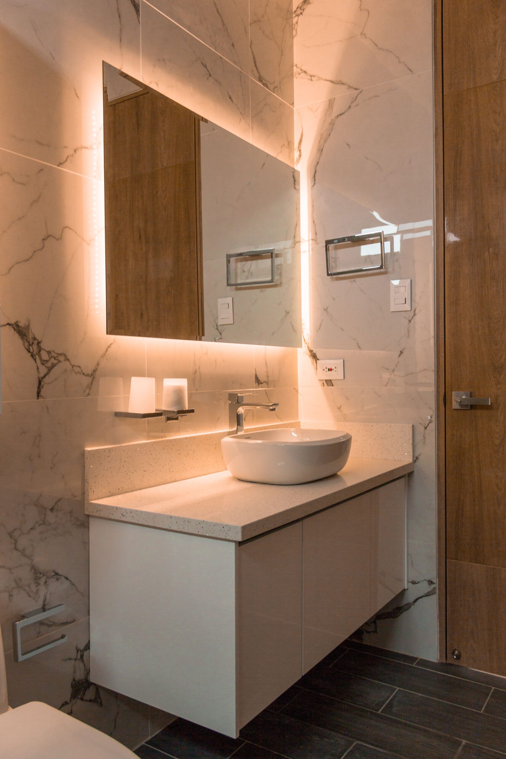 Modern white wall-mounted bathroom vanity with a vessel sink and a backlit mirror