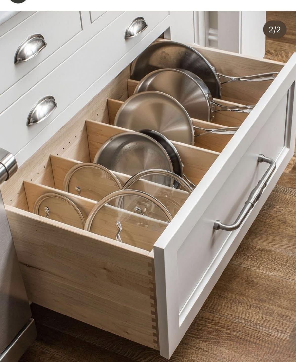 Deep drawer with wood dividers holding pans and lids in a white shaker cabinet