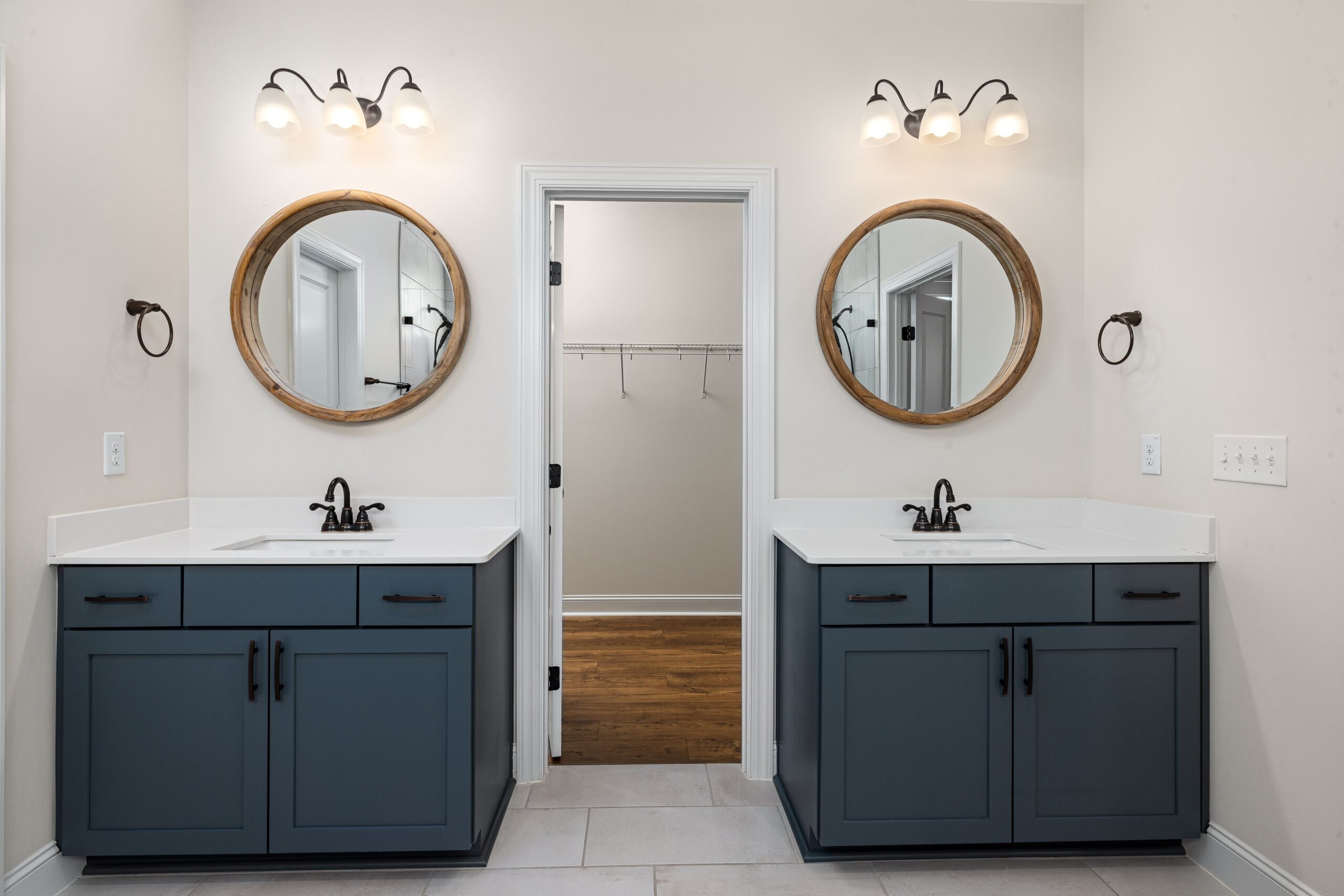 Two separate navy shaker bathroom vanities with round wood mirrors