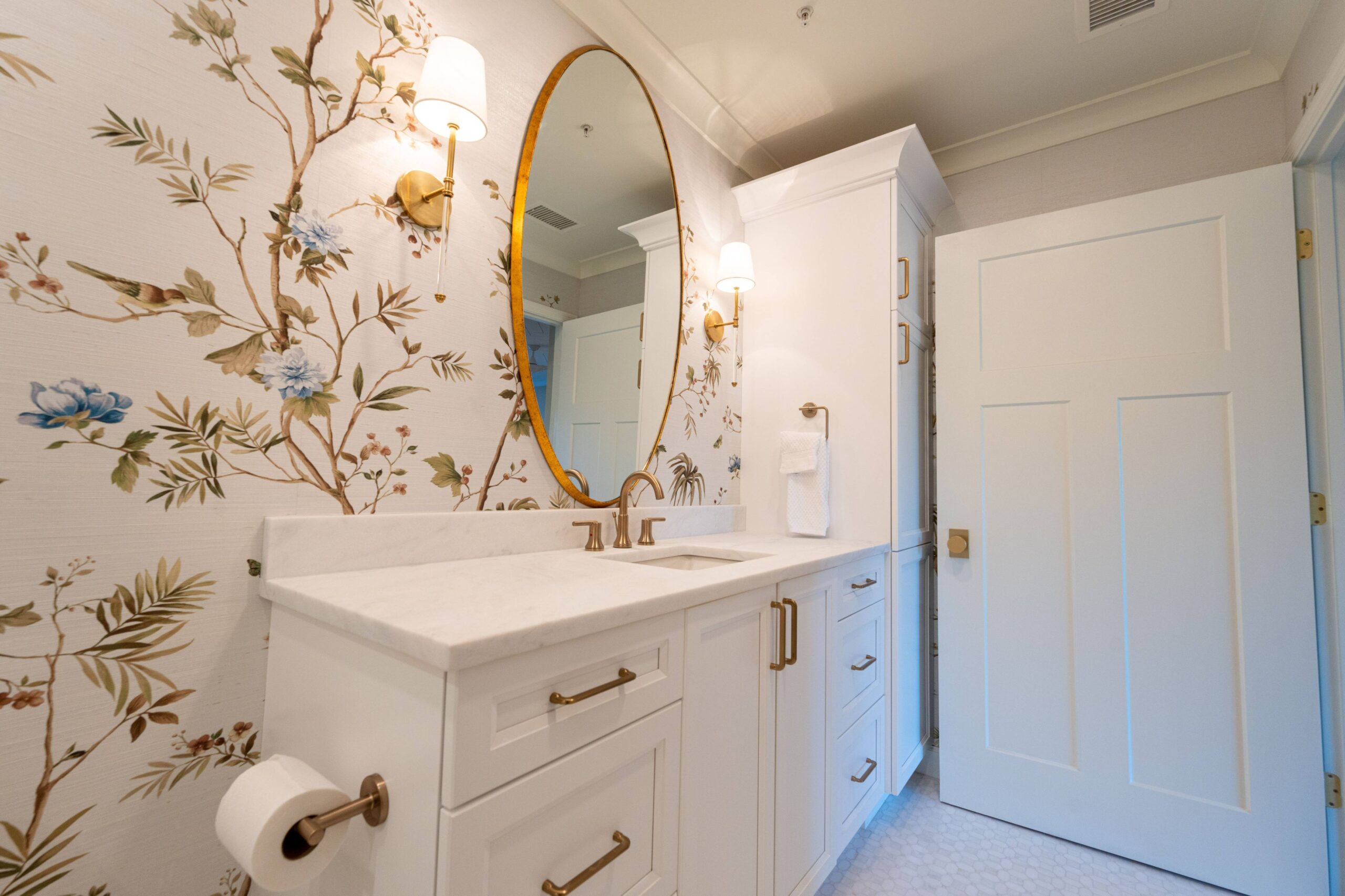 White bathroom vanity with brass pulls, a marble top and an arched gold mirror