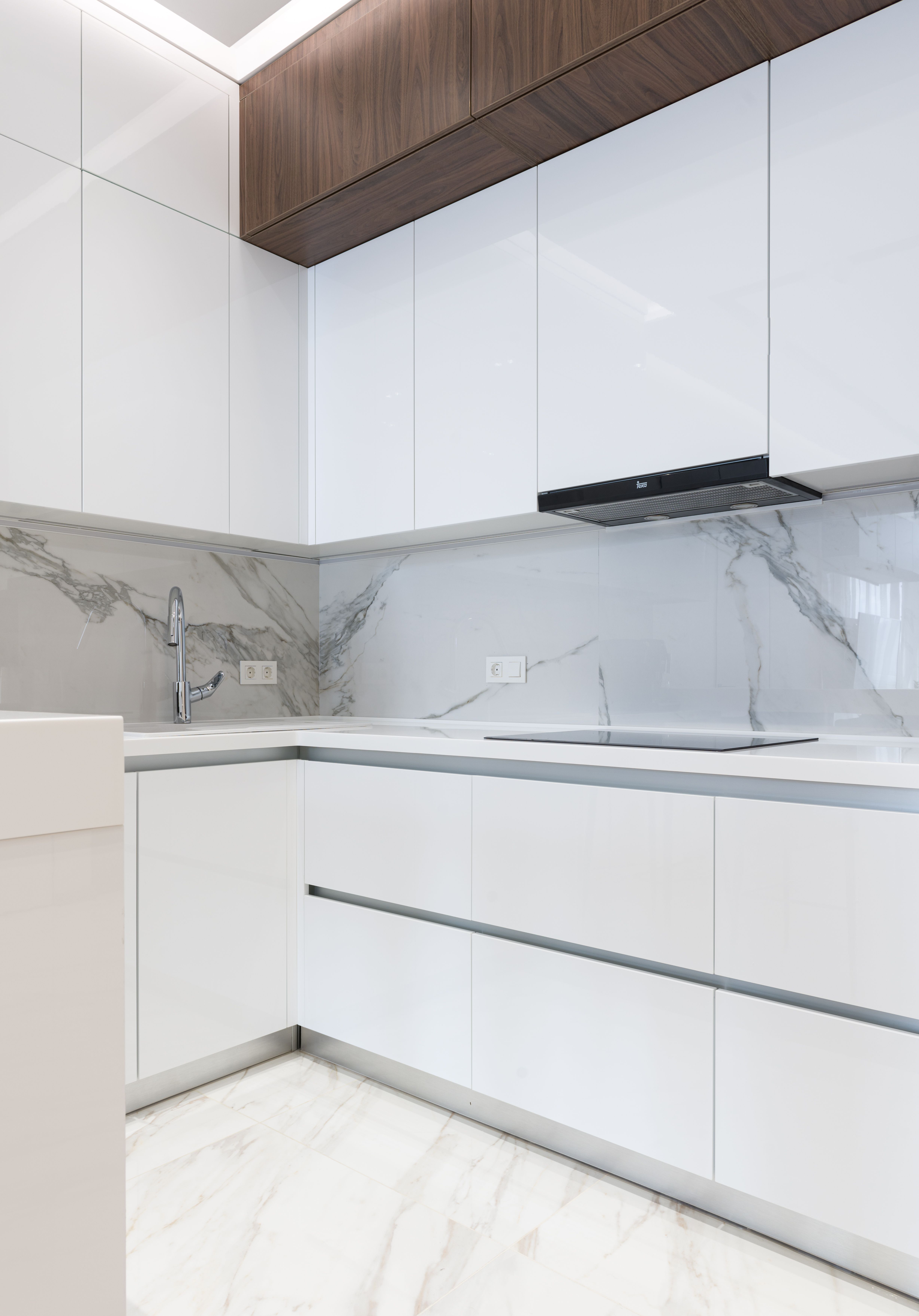 White veined countertop and full-height backsplash with white shaker cabinets and gold pulls