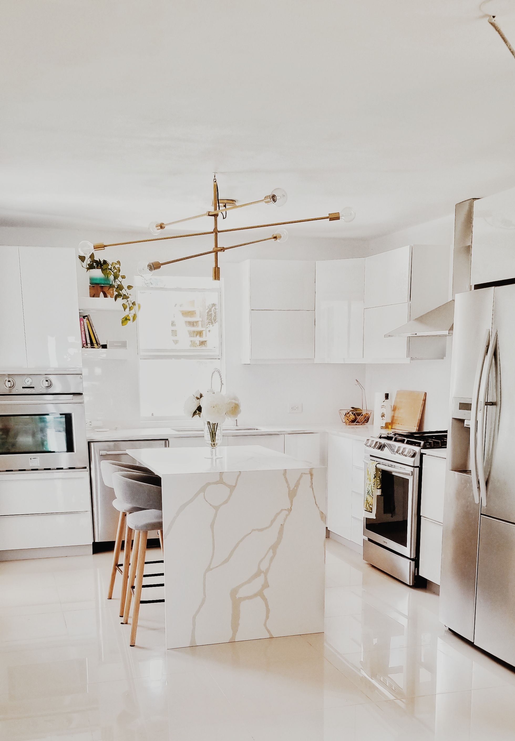 White kitchen with a white veined waterfall island countertop and brass pendant lights