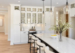 Glass-front white bar cabinets above a counter, next to a white kitchen island with stools