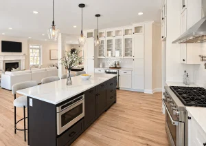 Open-plan white kitchen with a dark island, a gas range and the living room beyond