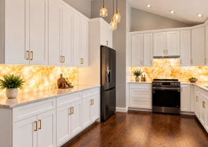 Sink run with white shaker cabinets, gold handles and an illuminated onyx-look backsplash