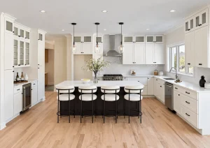 White L-shaped kitchen with an island, four white stools and glass-front upper cabinets